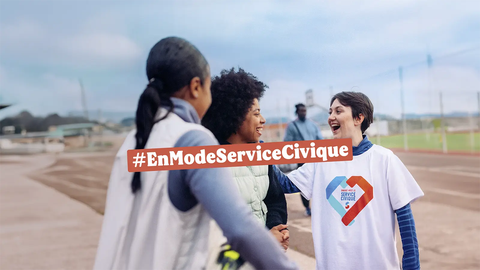 rs-visuel-header-youtube-campagne Three volunteers smile and shake hands outdoors, with a '#EnModeServiceCivique' banner crossing the scene in the foreground.